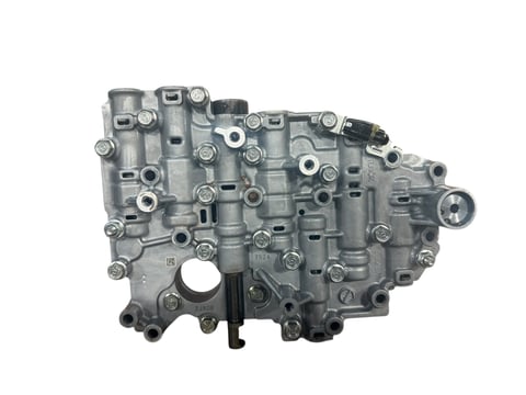 Gray metal transmission valve body with multiple ports, bolts, and solenoids on white background