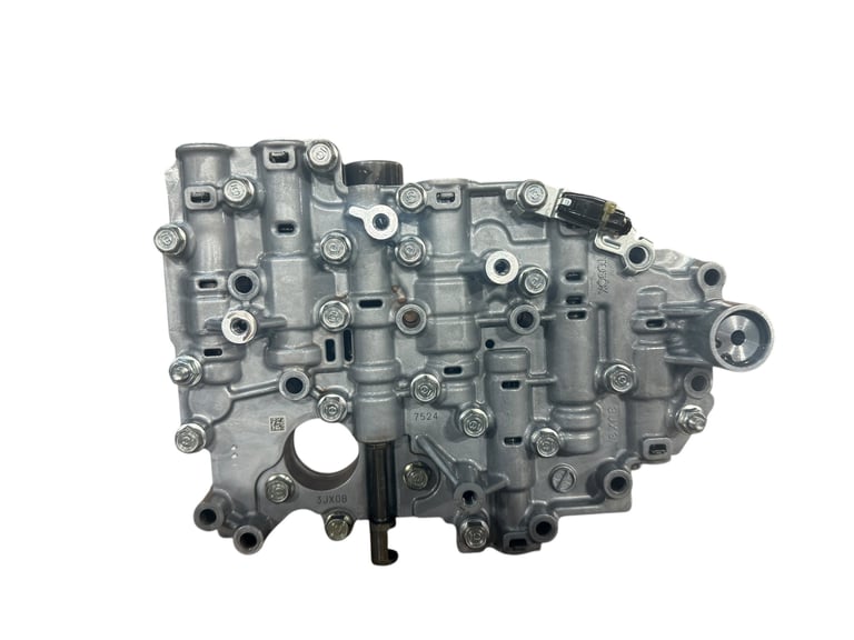 Gray metal transmission valve body with multiple ports, bolts, and solenoids on white background